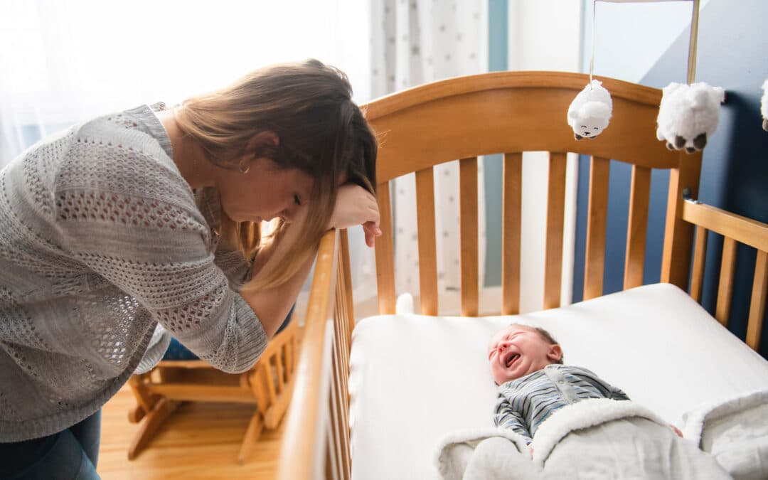 Mother leans on edge of crib while newborn cries.