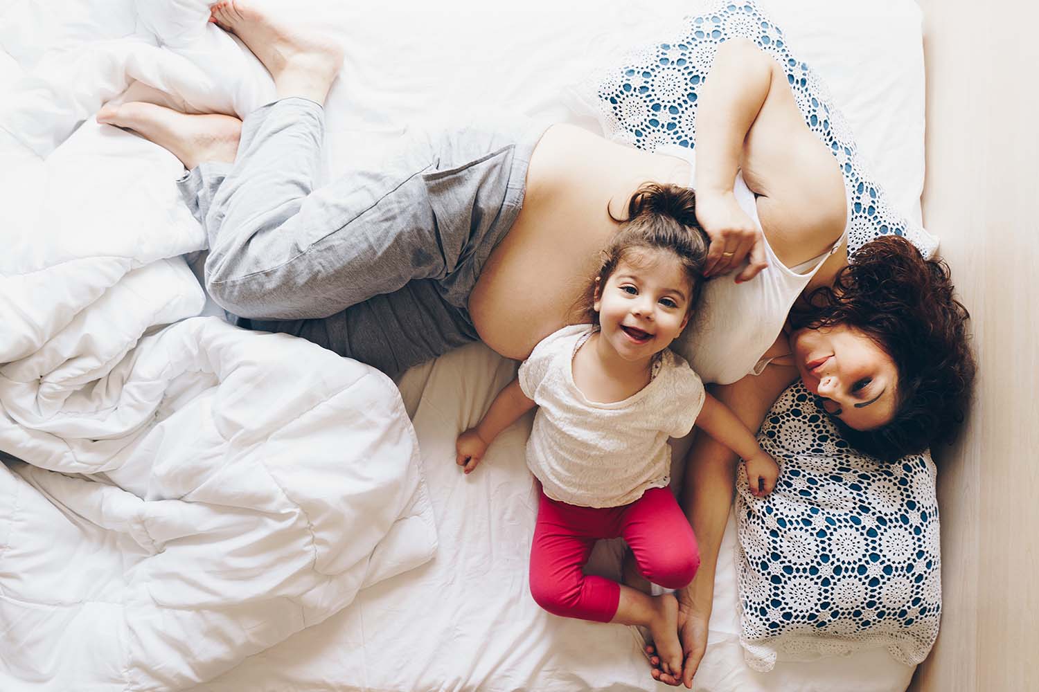 Pregnant woman reclining on a bed with a toddler smiling and leaning against her